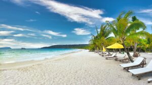 Entspannter Strand mit Palmen, Liegestühlen und Sonnenschirmen unter blauem Himmel, ideal für einen erholsamen Urlaub.