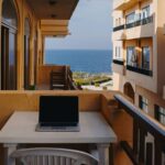 Balkon mit Blick auf das Meer, ausgestattet mit einem Laptop und Stühlen, ideal für Arbeit im Freien oder Entspannung mit Meeresblick.