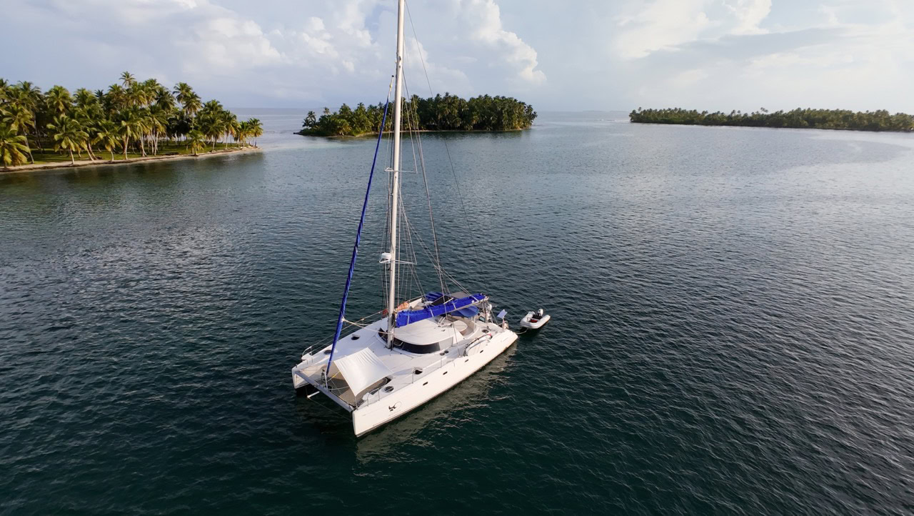 A sleek, luxury-equipped SV Monika catamaran floating peacefully in calm blue waters, surrounded by tropical islands with palm trees, ideal for private charter experiences.