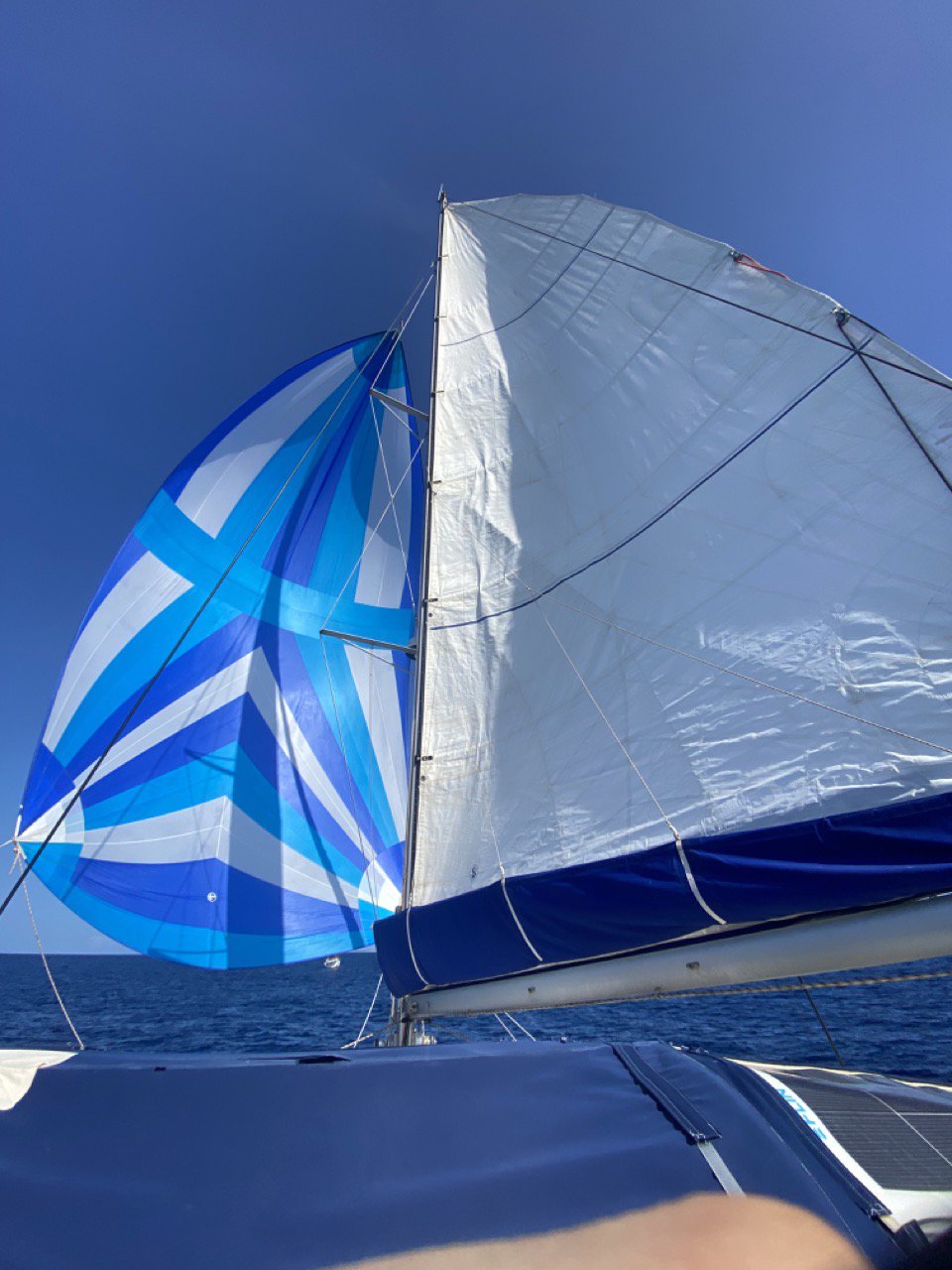 Close-up of a luxury catamaran with colorful sails on calm ocean waters under a clear blue sky.