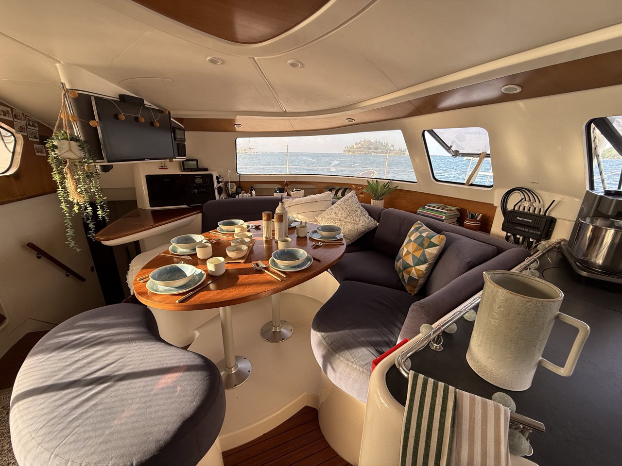 A cozy and stylish interior of the SV Monika luxury catamaran featuring a dining table set for a meal, plush seating, and large windows offering scenic views.