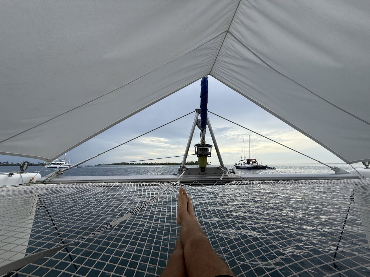 Experience the elegance of sailing on the luxury catamaran SV Monika, captured from the bow with the sail overhead and calm waters ahead.