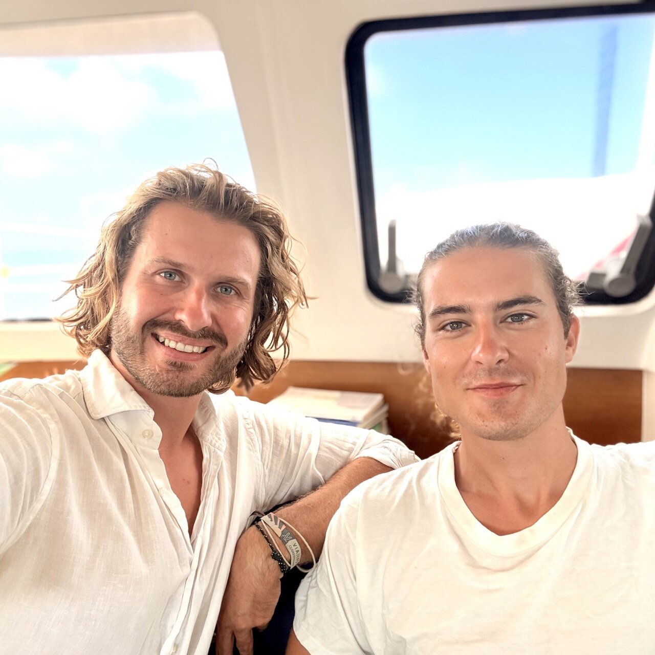 Two men smiling on the deck of the luxury catamaran SV Monika, enjoying a sunny day at sea.